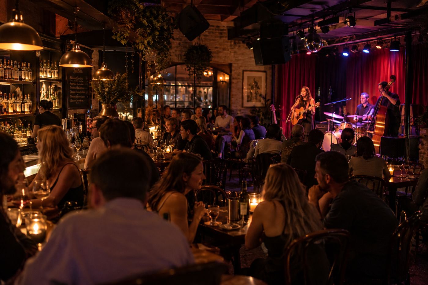 A packed bar room with a singer and band on a small stage under red curtains